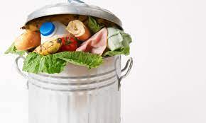 A metallic bin filled with edible food such as banana, leafy vegetable, tomato, a half eaten baguette... 